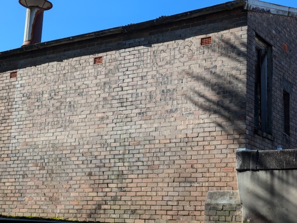 A brick wall with a very faint painted sign, no I don't know what it is for