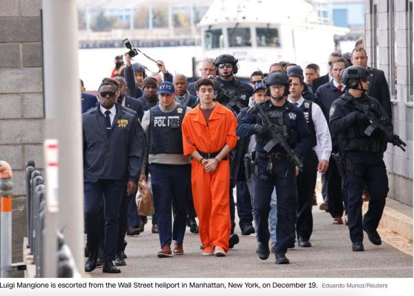 photo of luigi mangione in standard issue prison orange jumpsuit, escorted by a sea of NYPD dark blue. two rows behind him,  the corrupt former cop and mayor of nyc, Eric Adams, is strategically placed so any photos of Mangione will show him behind him.