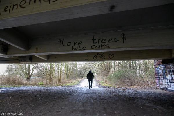 Spaziergänger unter dem Südschnellweg. Am Südschnellweg steht: „love trees hate cars“, Im Naturschutzgebiet Leinemasch sollen für den Bau einer nicht benötigten Standspur Bäume gerodet werden. Naturschützer*innen und Klimaaktivist*innen protestieren in der Leinemasch dagegen. Leinemasch, Hannover, 14.01.2024