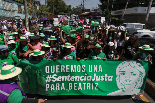 Protesters walk with a green banner demanding justice for Beatriz.