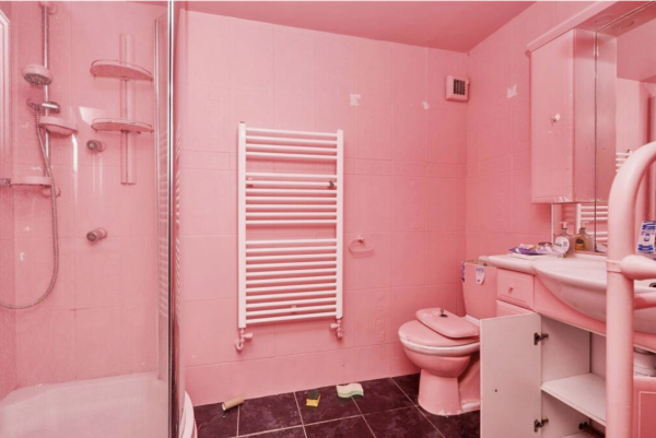 A bubblegum pink bathroom, the walls and ceiling and toilet are pink. There is stuff on the floor like a sponge and a toilet paper roll, and junk sitting on the sink.