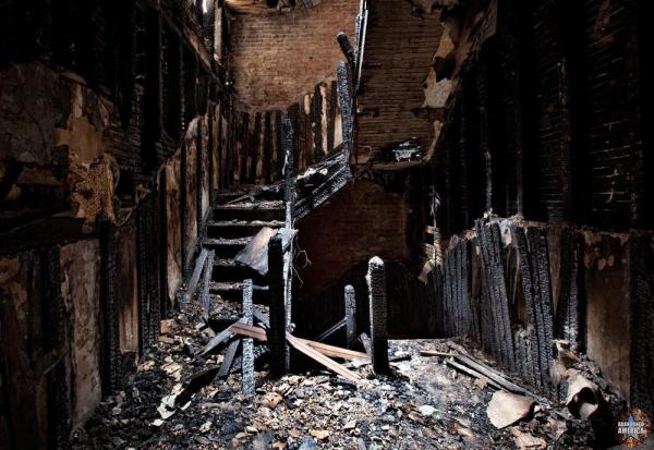 View of a blackened staircase. The railings and walls are charred and holes are visible on the underside of the steps