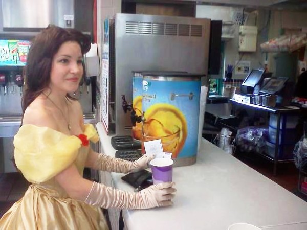 Someone in full Belle cosplay from Beauty and the Beast smiling and waiting for a drink refill at a Taco Bell.