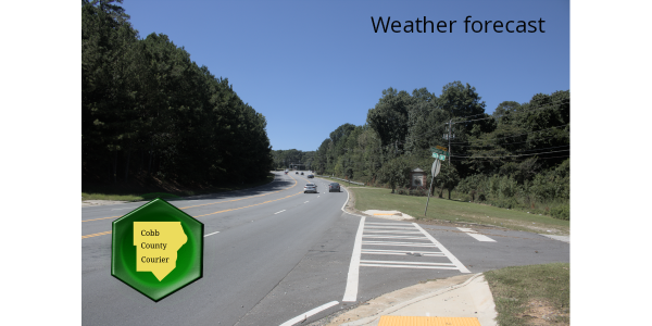 Veterans Memorial Highway in Mableton, Cobb County, Georgia, on a sunny, clear day, looking westward from a location near Oakdale Road and Discovery Boulevard.  Crosswalks across a side street are in the right foreground, and cars and trees are in the distance.
