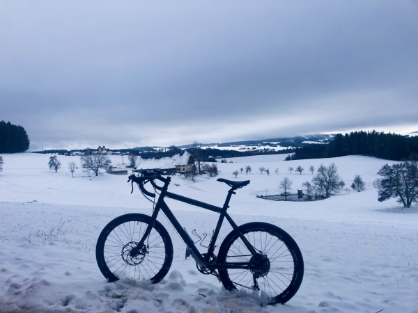 Ein Fahrrad steht vor einer verschneiten Winterlandschaft in den Bergen.