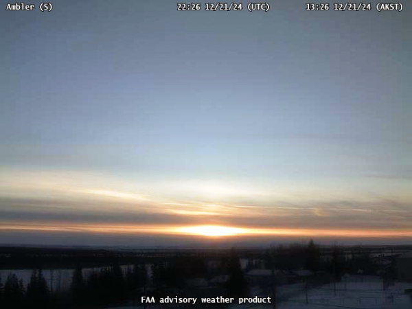 FAA webcam at the Ambler, Alaska airport looking due south, showing some high clouds along the horizon but with the sun shining through. 