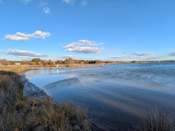 Photo of a clear, cold and windy winter solstice afternoon on Harris Creek, sun behind us bathes the scene in golden afternoon light. Sky is a deep perfect blue with scattered puffy white clouds.Marsh is brown and just doesn't want to be bothered right now. Creek water is rippled and reflects the sky and clouds.