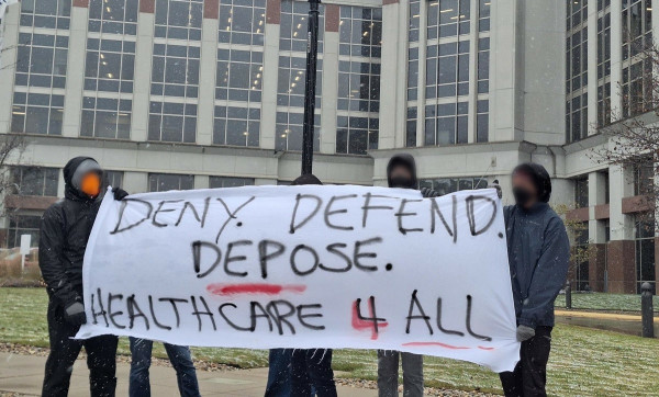 Protesters in front of medical building hold banner reading, "Deny, Defend, Depose, Healthcare 4 All."