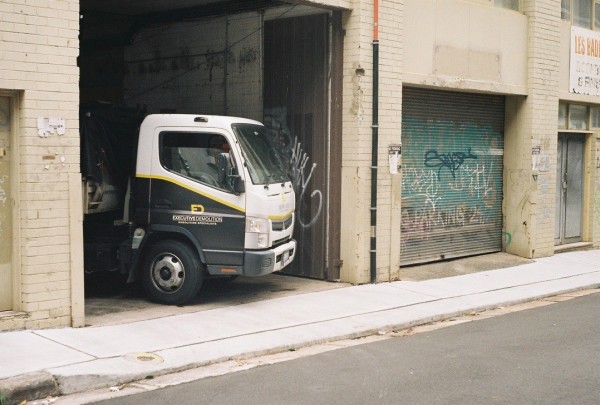 A small van poking its nose out of a small industrial building, into a laneway.