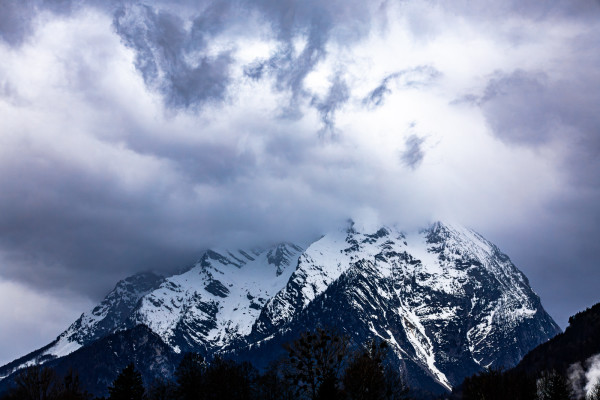 Blick auf einen großen, verschneiten Berg. Der Gipfel steckt mitten in den Wolken. Diese haben sich intensiv zusammengebraut und bedecken den gesamten Himmel. Es herrscht eine düstere Stimmung.