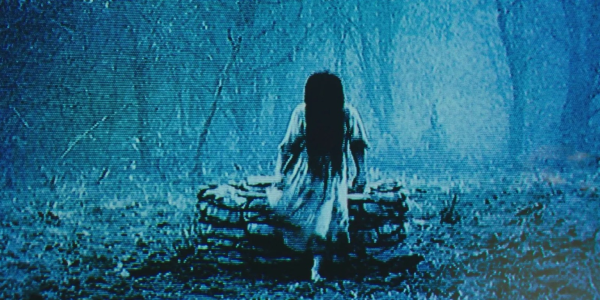 Screen grab from the horror movie “the ring“. It’s grainy blue tinted and there’s an old Wishingwell and a creepy girl just came out out of it, and her hair is long and completely covering her face.