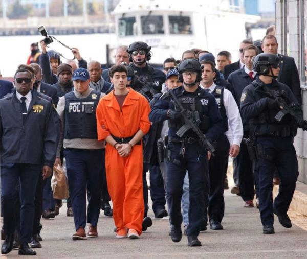 Luigi Mangione in an orange jumpsuit being escorted by a horde of law enforcemennr