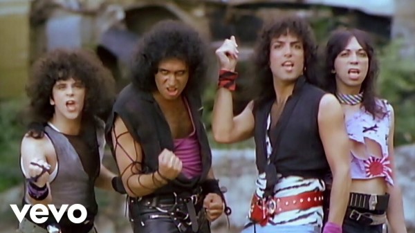 Screenshot of the band kiss from the video for “lick it up”. They all have brunette, perms, and punky gathered clothing in big belts.